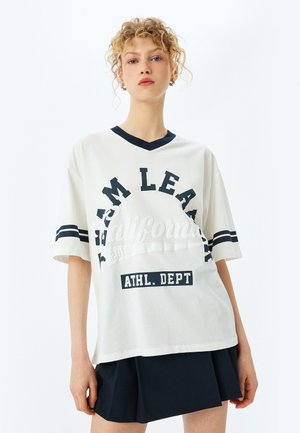 T-shirt bianca in cotone con scollo a V navy, con bold nero "TEAM LEARN" e "ATHL. DEPT", accentuata da maniche a righe.