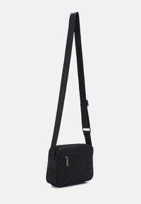 Černá obdélníková crossbody taška s přední kapsou na zip, nastavitelný popruh s vyraženým textem "Valentino".