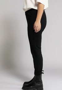 Černé zúžené kalhoty s elastickým pasem, bočními kapsami a slim fit. V kombinaci s černými kotníkovými botami se silnou podrážkou.