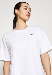 T-shirt bianco in cotone con scollatura a girocollo e maniche corte, dotato di un piccolo logo FILA nero e rosso sulla parte sinistra del petto.