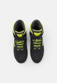 Baskets montantes noires avec des accents jaune fluo, un matériau texturé, des lacets proéminents et une sangle de maintien autour de la cheville.