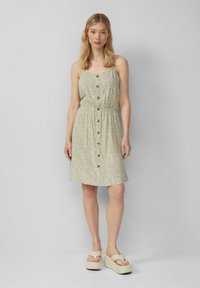 Grünes Blumenkleid mit tailliertem Schnitt, Knopfverschluss vorne und Spaghettiträgern. Getragen mit leichten Plateau-Sandalen. Weicher Stoff und lockere Passform.