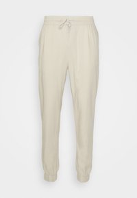 Beige linnes joggers med elastisk midjeband, justerbar dragsko och muddar vid anklarna. Slät textur, avslappnad passform, avslappnad design.