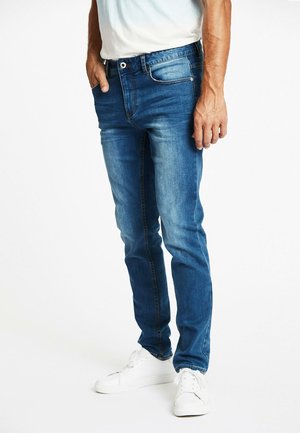 Jeans de mezclilla azul con corte slim, que cuentan con cinco bolsillos, ligero desgaste y costura en contraste. Combinados con zapatillas blancas.