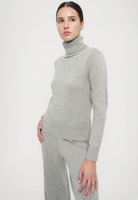 Grauer gerippter Rollkragenpullover aus weichem Stoff, mit taillierten Schnitt und einem gestickten Logo am Saum.