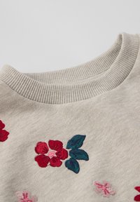 Lichtbeige sweatshirt met florale borduursels in rood, roze en groen. Ronde geribbelde halslijn en zachte textuur.