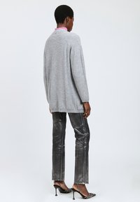 Suéter gris de manga larga con un corte holgado y tejido texturizado, combinado con pantalones negros brillantes de pierna recta con rayas laterales y dobladillos deshilachados.