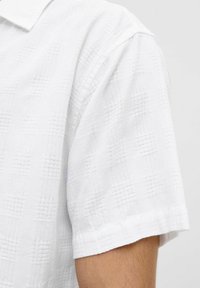 Camicia bianca a maniche corte con un motivo testurizzato, caratterizzata da un sottile design a griglia. Tessuto morbido con colletto classico e orlo pulito.
