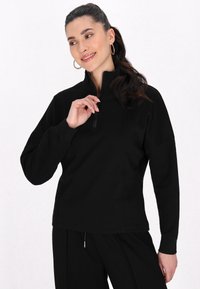 Pullover nero con zip, maniche lunghe e colletto alto. Realizzato in tessuto morbido, presenta una vestibilità rilassata e cuciture sottili.