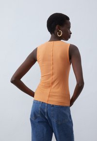 Slim-fit orange ribbed tank top with a crew neckline and center seam detail, paired with high-waisted blue denim jeans.