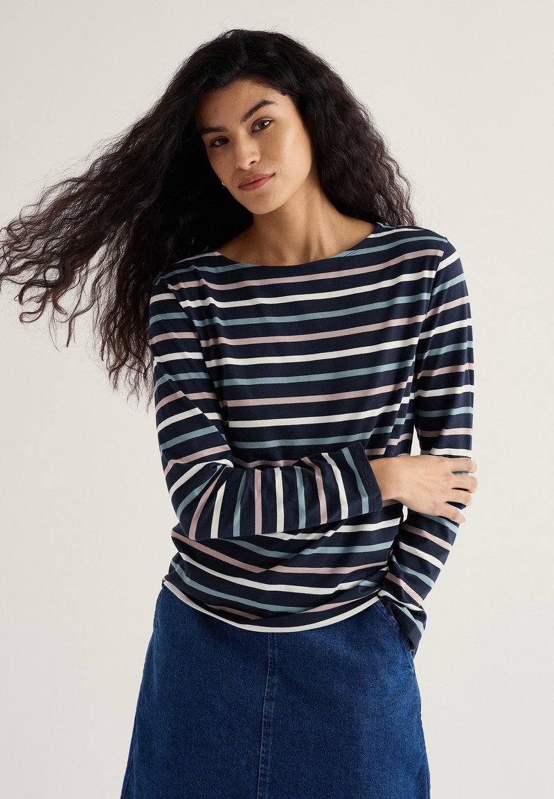 Maglietta a maniche lunghe con righe orizzontali in blu navy e pastello. Tessuto liscio, ampio scollo rotondo e vestibilità rilassata, indossata con una gonna di jeans.