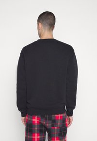 Sudadera negra con cuello redondo y mangas largas, con una textura suave. Combinada con pantalones de cuadros en rojo, negro y amarillo.