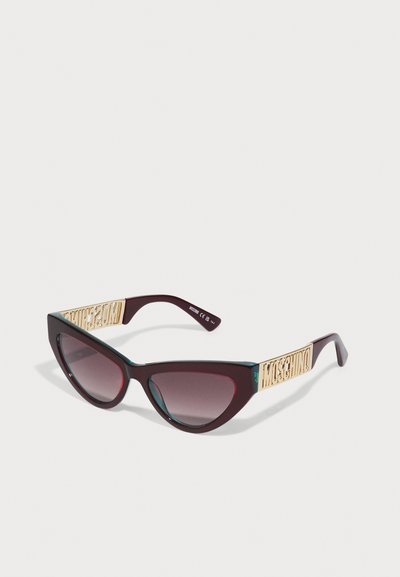 Ochelari de soare cu formă de ochi de pisică, cu rame de un burgundy închis, lentile degradée și logo-ul „Moschino” de ton auriu pe temple. Textură netedă și design elegant.