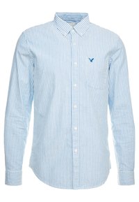 Chemise à manches longues à rayures bleu clair et blanc, col boutonné, poche poitrine et petit logo sur le côté gauche. Texture de tissu douce.
