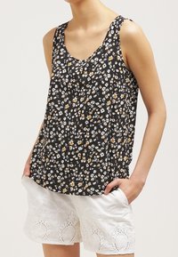 Débardeur noir avec un motif floral en blanc et jaune, présentant un col arrondi et une coupe ample, associé à un short blanc brodé.