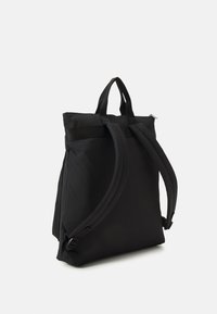 Svart nylonryggsäck med en strukturerad form, två justerbara axelremmar och ett handtag på toppen; har en minimalistisk design och dragkedjestängning.