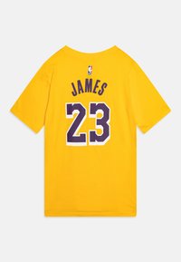 Keltainen puuvillapaita lyhyillä hihoilla, jossa takana on teksti "JAMES" ja numero "23" violetilla, NBA-logo tekstin yläpuolella.