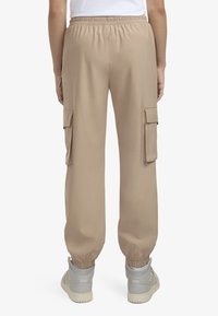 Beige cargo kalhoty s elastickým pasem a manžetami, které mají dvě boční cargo kapsy a hladkou, lehkou tkaninu.