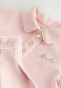 Hellrosa Poloshirt mit weißer Paspelierung, goldenen Druckknöpfen und besticktem "Baker by Ted Baker" Logo auf Brust und Manschette.