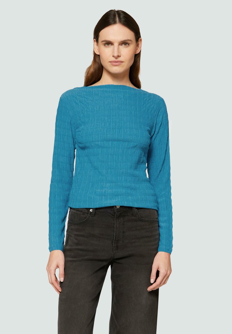 Haut à manches longues en texture côtelée de couleur bleu vif, en tissu extensible, associé à un jean en denim foncé, silhouette ajustée, encolure ronde.