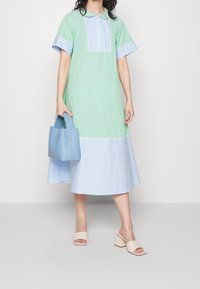 Raidallinen mekko vihreän ja sinisen sävyissä, jossa on kauluskansi ja lyhyet hihat. Vaaleansininen olkalaukku. Nude-väriset korkokengät. Silkkinen rakenne.