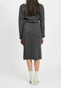 Šedé pletené šaty s dlouhými rukávy, obepínající silueta, po kolena. Modelka na sobě má bílé kotníkové boty, vlasy má stažené rovně dolů.