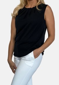 Mustaton hihaton paita, jossa on drapattu kaula-aukko, pehmeä kangas ja pyöristetty helma. Yhdistetty valkoisiin kaarrettuihin housuihin, joissa on sivutaskut.