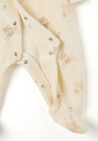 Monos de color crema con estampado de animales que presentan mapaches y conejos. Hecho de tela suave, con cierres a presión a lo largo del costado y diseño con pies.