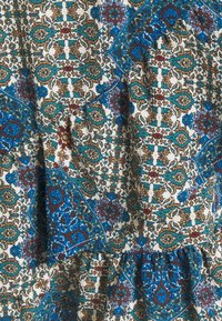 Tissu à motifs multicolores présentant des motifs complexes bleus, rouges et bruns sur fond blanc. Texture froncée à l'ourlet.