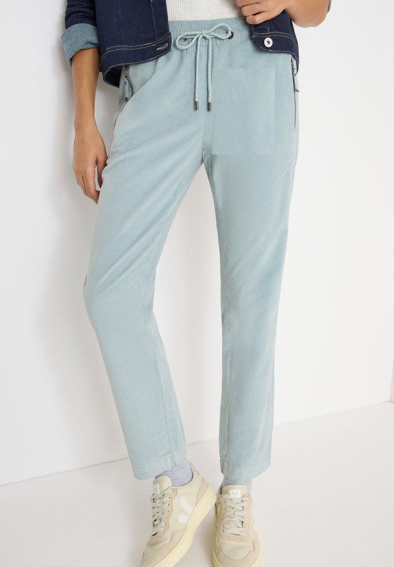 Pantaloni di stoffa leggeri blu chiaro, morbidi, con vita elasticizzata e coulisse, tasche laterali e design a gamba affusolata. Abbinati a sneaker chiare.