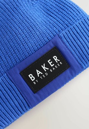 Modrá pletená čiapka s rebrovanou textúrou. Obsahuje obdĺžnikový čierny štítok s bielym textom "BAKER BY TED BAKER" jasne zobrazeným.