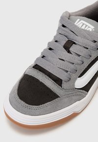 Chaussure de skate en daim gris avec accents noirs, bande latérale blanche et semelle en caoutchouc texturée ; équipée de lacets plats gris et boîte à orteils perforée.