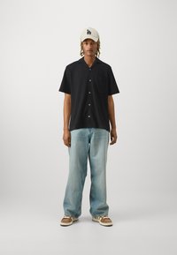 Mustade lühikeste varrukatega nööbiga särk, millel on rinna-tasku, kombinatsioon helesiniste avarate teksade ja beežide tossudega. Valge müts tekstiga.