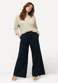 Haut rayé beige clair à manches trois-quarts et pantalon large marine avec des accents de boutons sur le côté. Tissu texturé.