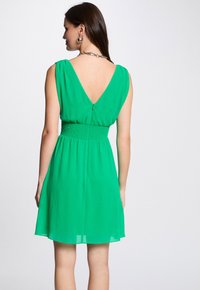 Groene mouwloze jurk met een V-hals aan de achterkant, smocktail, lichtgewicht stof en een vloeiende rok die boven de knie valt.