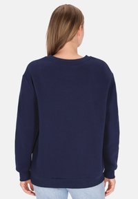 Sudadera azul marino con mangas largas, puños acanalados y cuello redondo. Tejido suave, corte holgado, detalles mínimos.