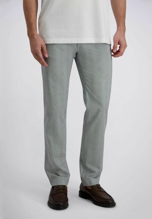 Homme portant un pantalon de costume gris clair et des mocassins en cuir brun foncé, debout devant un fond uni clair.