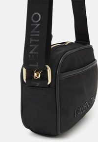 Svart nylon axelväska med en guldfärgad dragkedja, med en texturerad logotyp och en bred justerbar rem med "VALENTINO" tryckt i grått.