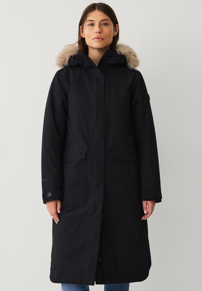 Parka nera lunga realizzata in tessuto resistente all'acqua, con cappuccio foderato in pelliccia, tasche frontali e taglio dritto. Design minimalista con branding discreto.
