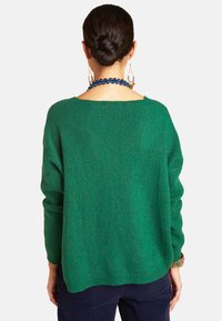 Grüner Strickpullover mit lockerer Passform, weiter Ausschnitt und langen Ärmeln. Der Stoff hat einen subtilen Glanz und zeigt eine weiche Textur.
