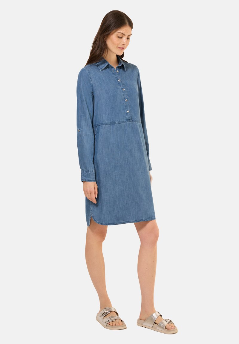 Robe chemise en denim à manches longues, avec un devant à boutons, un col pointu et un ourlet arrondi. Portée avec des sandales à glissière métalliques.