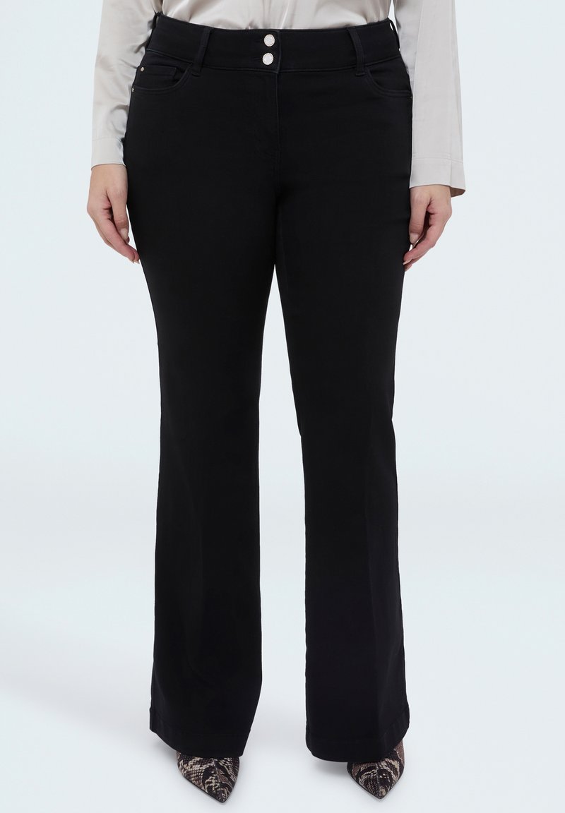 Musta liehuva housut, joissa on sileä kangas, kaksi etunappia, sivutaskut ja hienovarainen kiilto, yhdistetty teräväkärkisiin kenkiin.