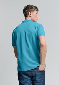 Turquoise poloshirt met een klassieke kraag, korte mouwen en een soepele, lichte stof. Heeft een ontspannen pasvorm met zijsplitten.
