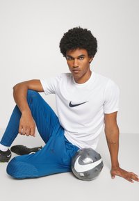 Nike Sportbekleidung umfasst ein weißes kurzärmeliges Shirt und eine blaue Hose mit gemusterten Akzenten, kombiniert mit einem grauen Fußball.