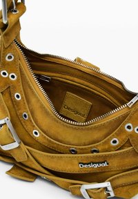 Smeđa suđena torba sadrži srebrne očnice, patentne zatvarače, kopče i vidljivo "Desigual" brendiranje na prednjoj i unutarnjoj džepu.