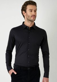 Donkerblauwe overhemd met een klein geometrisch patroon. Heeft lange mouwen, een kraag en subtiele knoopaccenten.