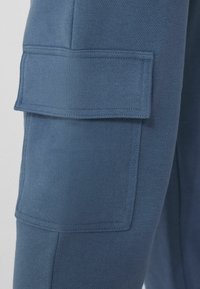 Námořnické modré tepláky s hladkým povrchem, elastickým pasem a dvěma velkými cargo kapsami s klopovými uzávěry na stranách.