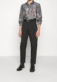 Langärmliges Hemd mit dunklem Blumenmuster; schwarze Slim-Fit-Hose; kombiniert mit schwarzen Leder-Stiefeletten; insgesamt glänzende Textur.