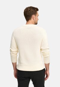 Maglione lavorato a maglia di colore crema con vestibilità morbida, scollatura rotonda e polsini a coste. Texture liscia con una trama leggermente allentata.