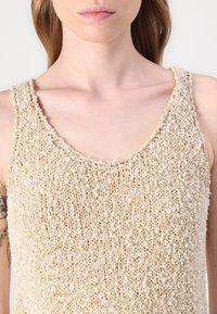 Top de tanque texturizado en beige y crema, con escote redondeado y tela suave tejida. Fibras sueltas notables y un ajuste relajado.
